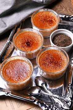 four desserts in small glass dishes on a silver tray with spoons and utensils