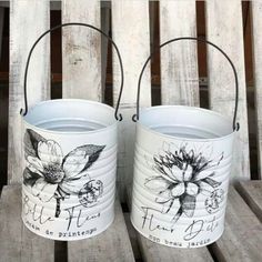 two buckets with flowers painted on them sitting on a wooden table next to each other