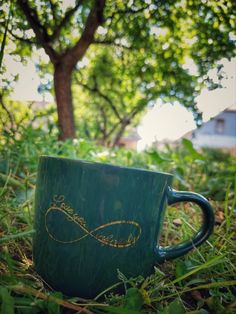 a green coffee cup sitting in the grass under a tree with a gold heart drawn on it