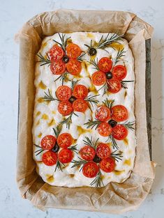 an uncooked pizza with tomatoes on it in a cardboard box sitting on a counter