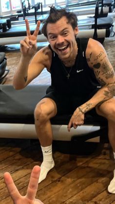 a man sitting on top of a gym floor making the peace sign with his hand