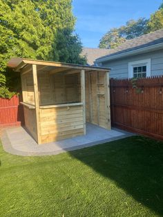 a wooden shed sitting on top of a lush green field next to a fenced in yard