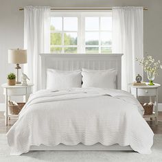 a bed with white linens and pillows in a bedroom next to a large window