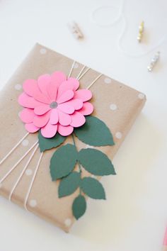 a gift wrapped in brown paper with pink flower on top and green leaves attached to it