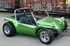 a green sports car is parked in front of some train tracks with graffiti on it