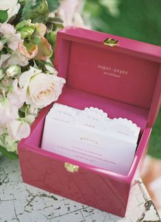 an open pink box sitting on top of a table next to white flowers and greenery