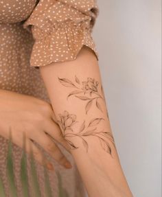 a woman's arm with flowers on it and leaves in the middle, while she is wearing a polka dot dress