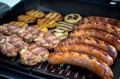 several sausages and hamburger patties are cooking on a grill with other food items