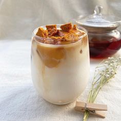 a glass filled with liquid next to a wooden spoon and some dried flowers on a table