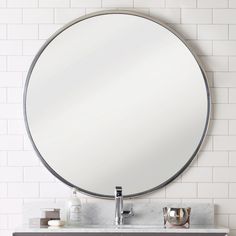 a round mirror on the wall above a sink in a bathroom with white tiled walls