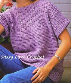 a woman sitting on the ground wearing a purple knitted sweater and holding a flower in her hand