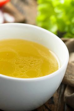 a white bowl filled with yellow liquid next to lettuce and tomatoes on the table