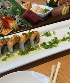 sushi on a white plate with chopsticks next to it and another dish in the background