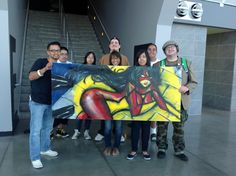 a group of people standing next to each other in front of stairs holding up a painting