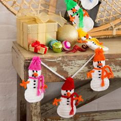 an assortment of knitted snowmen and gifts on a wooden table next to a clock