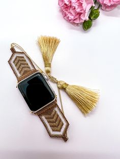 an apple watch with tassels on it next to flowers and pink carnations