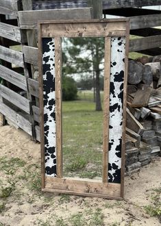 a cow print mirror sitting on top of a pile of wood next to a fence