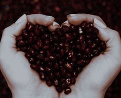 two hands are holding some beans in the shape of a heart