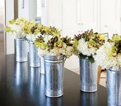 four metal buckets with flowers in them on a table