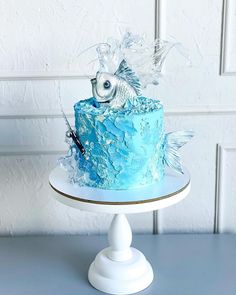 a blue frosted cake with fish on top sitting on a white pedestal in front of a white wall