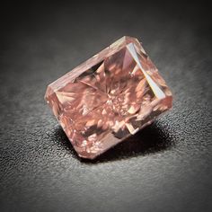 a fancy pink diamond sitting on top of a table next to a black surface with light coming through it