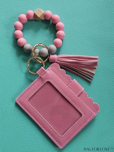 a pink card case with tassels and a keychain on a turquoise background