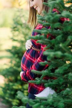 a woman standing in front of a tree looking down at her pregnant baby bumping it's belly