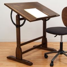 a wooden drafting table with a black chair next to it and a white piece of paper on top