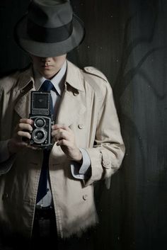 a man in a trench coat and hat holding an old camera