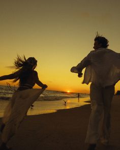 two people on the beach at sunset with their hair blowing in the wind as the sun sets