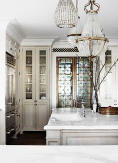 a chandelier hanging from the ceiling in a kitchen with marble counter tops and white cabinets