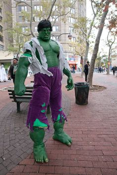 a man dressed as the incredible hulk stands in front of a bench on a brick sidewalk