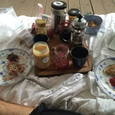 two plates with food on them sitting on a bed next to cups and saucers