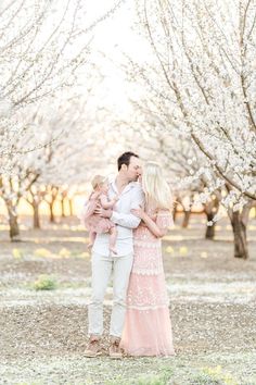 a man and woman are holding their baby while standing in front of some blossoming trees