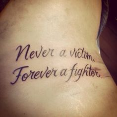 a woman with a tattoo saying never a victim, forever a fighter on her lower back