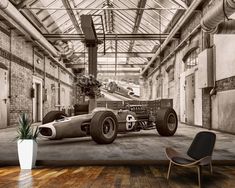 an old race car is parked in a warehouse with exposed pipes and large windows on the ceiling