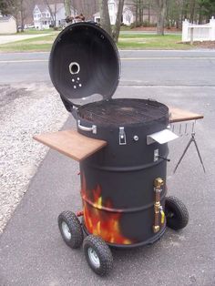 an outdoor bbq grill with wheels on the side and fire burning in the back