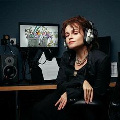 a woman wearing headphones sitting in front of a computer desk with speakers on it