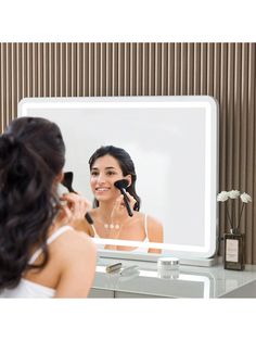 a woman is looking at her reflection in the mirror while she brushes her hair with an electric blow dryer