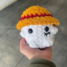 a hand holding a small crocheted toy with a hat on it's head