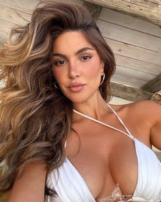 a beautiful woman in a white dress posing for the camera with her long hair blowing in the wind