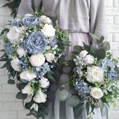 two bridesmaids holding bouquets of blue and white flowers in front of a brick wall