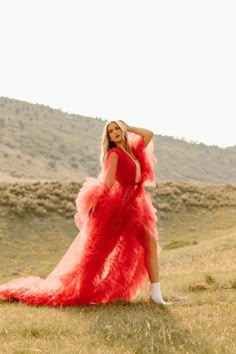 a woman in a red dress is standing on the grass with her hands behind her head