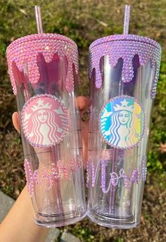 two tumblers with pink and purple designs on them are being held by someone's hand