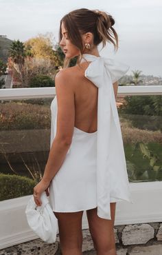 a woman wearing a white dress and holding a purse looking out over the water from her balcony