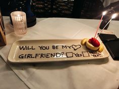 a sign that says, will you be my girlfriend? on a plate next to a cell phone