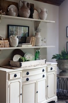 a white cabinet with vases and other items on it's shelves in a living room