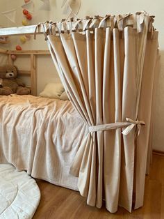 a teddy bear is sitting on the floor in front of a bed with drapes