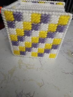 a small basket with yellow and purple squares on the inside is sitting on a counter