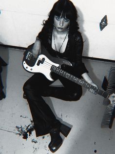 a black and white photo of a woman with a guitar in her lap, sitting on the floor